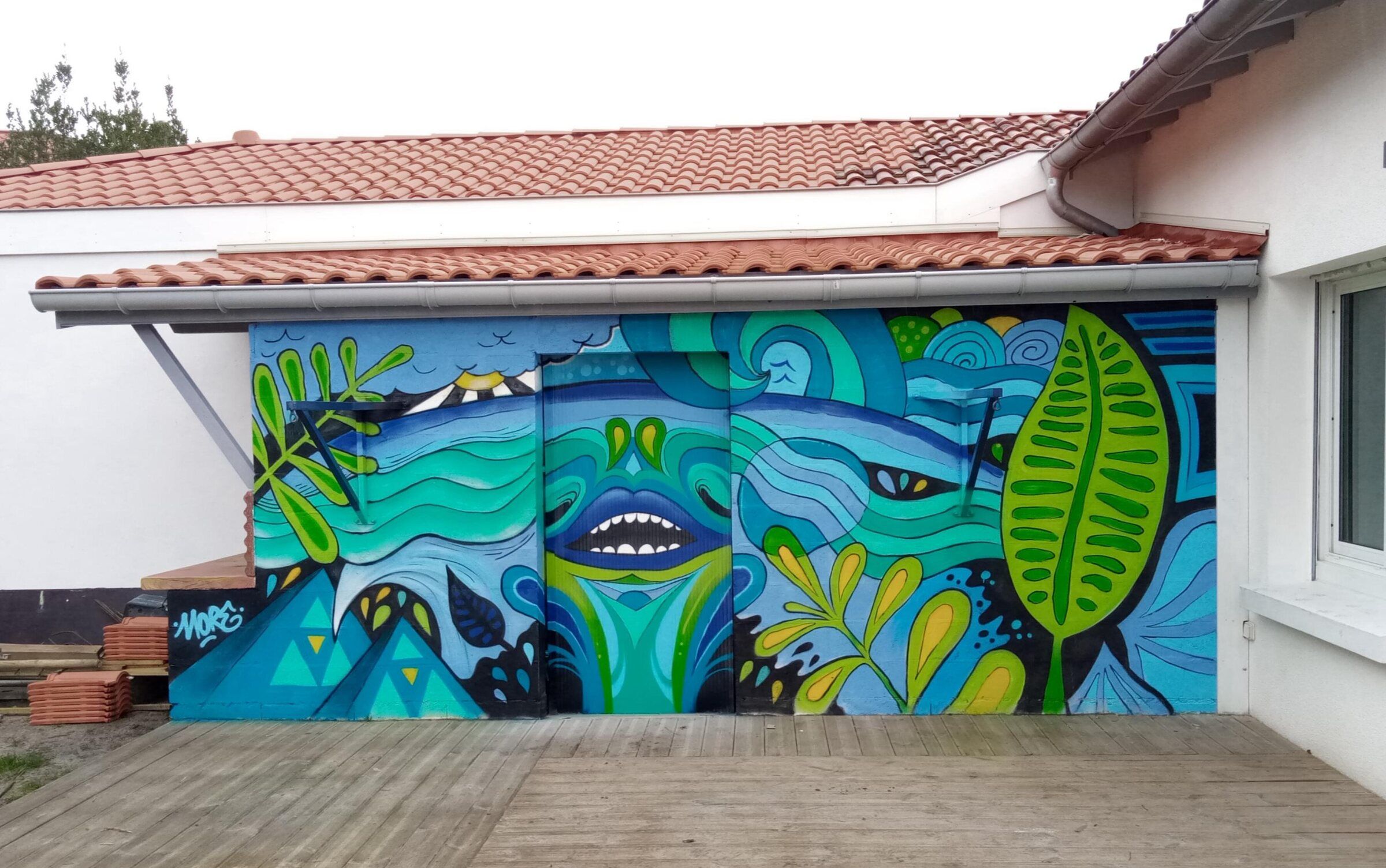 Mur extérieur d'une maison peint de vagues, de feuillages et de motifs graphiques bleus et verts