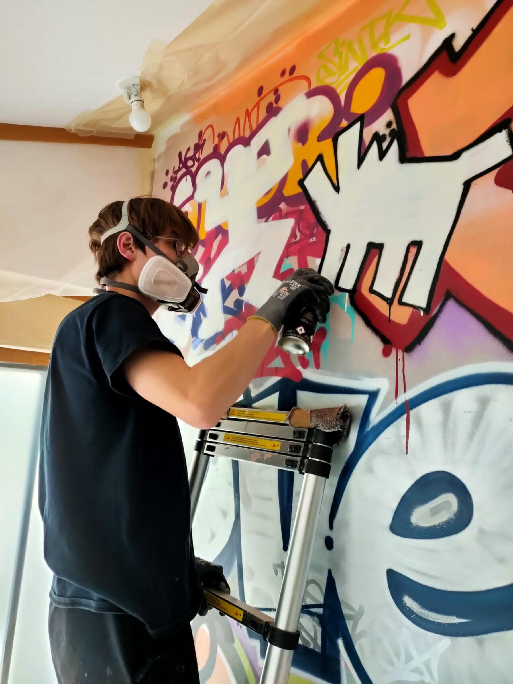 Simon Gaillourdet en train de peindre une fresque à la bombe, sur un escabeau