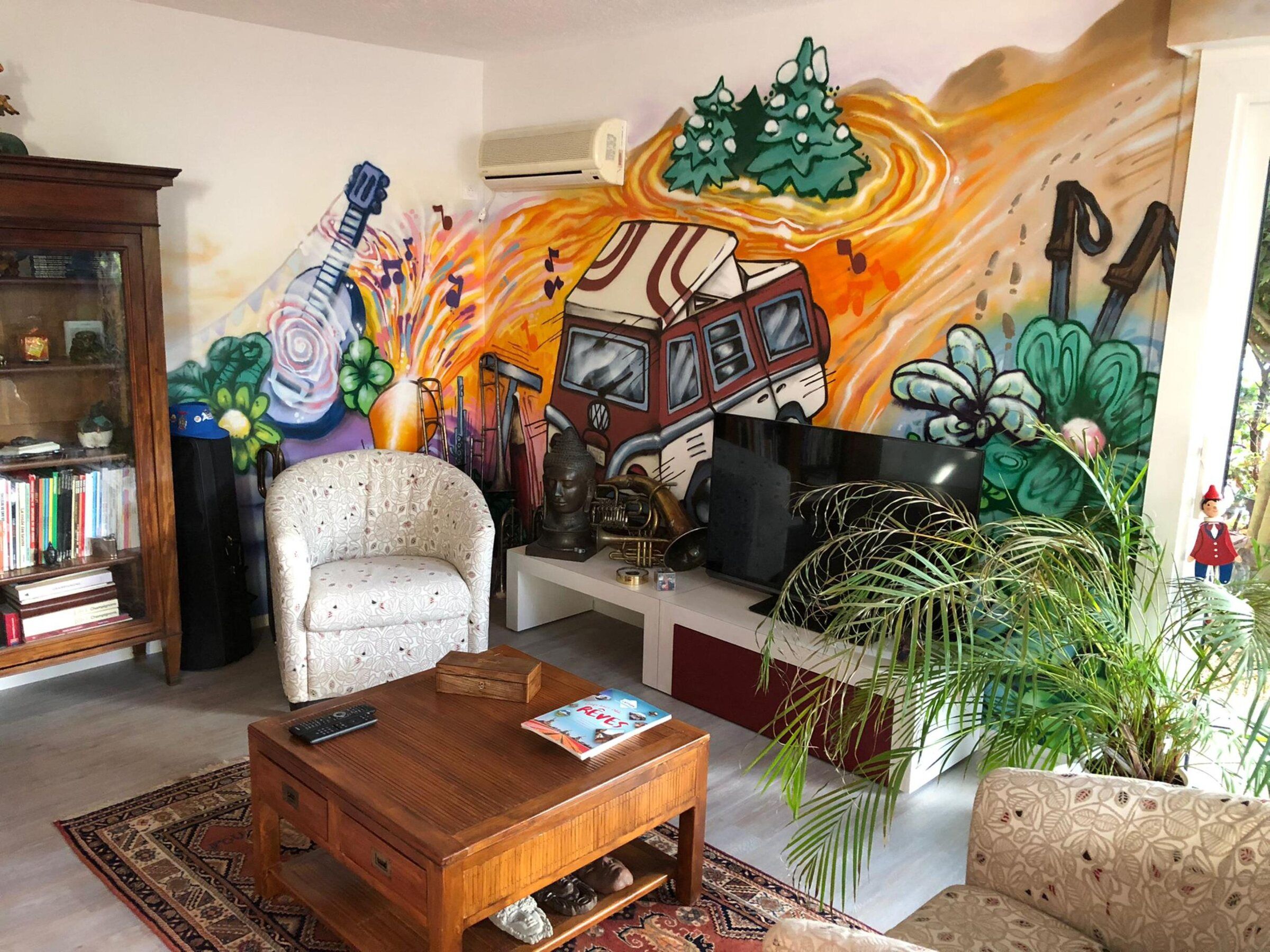 Fresque courant sur les murs d'un salon meublé : guitare, trompette, combi Volkswagen et végétation colorée